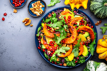 Healthy salad with baked pumpkin slices, red cabbage, avocado, lettuce, arugula, pomegranate and lnuts. Vegan vegetarian eating, comfort food. Gray table background. Top view