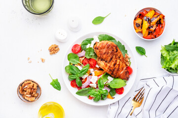 Healthy salad with grilled paprika and chicken, feta cheese, cherry tomatoes, walnut, red onion and lettuce, white table background, top view