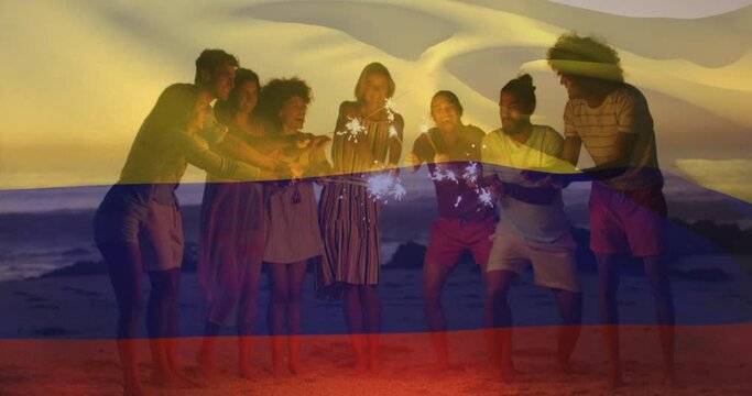 Animation of colombian flag waving over diverse friends with sparklers enjoying at beach