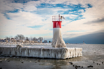 Red and white lighthouse on pier covered with snow and ice during the winter