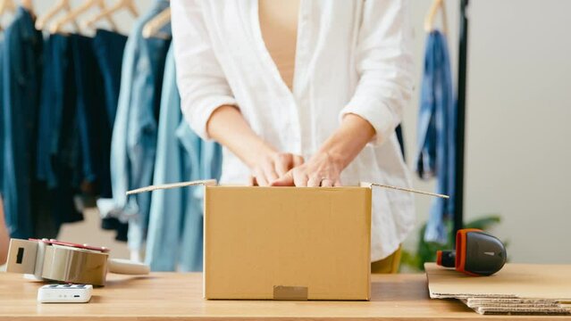 Close up on hands of woman running online fashion business packing pair of denim jeans into box and sealing for distribution