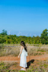 A Girl stands against the wind turbine generate electricity, fan fields on the green grass over the blue clouded sky in Ea H'leo district, Dak Lak province, Vietnam.