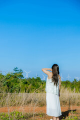 Naklejka na ściany i meble A Girl stands against the wind turbine generate electricity, fan fields on the green grass over the blue clouded sky in Ea H'leo district, Dak Lak province, Vietnam.