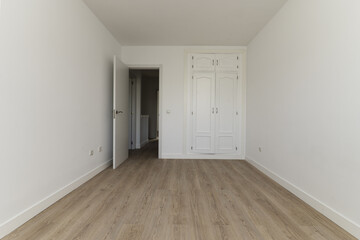 Empty bedroom with a built-in wardrobe with two white wooden doors, skirting boards of the same...