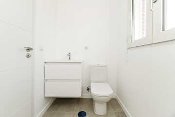 Small bathroom in a house with a white porcelain sink hanging on the wall with wooden cabinets of drawers