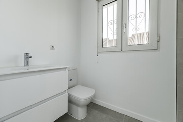 Fototapeta na wymiar Small bathroom in a house with white porcelain sink hanging on the wall with wooden drawers and white aluminum window with exterior bars