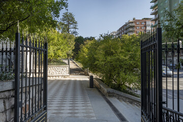 Access to an urban park with dirt paths, stone stairs, metal fence and lots of trees