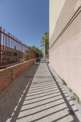 Obraz premium Pedestrian walk between buildings of a residential housing colony built in the 1950s and a metal fence that creates shade