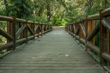 A bridge with railings made of wooden logs, planks in a park with lots of trees