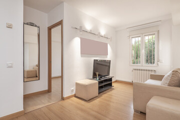 Small living room of a house with beige fabric sofa, barred window and access to a small hallway with access to other rooms