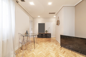 Small living room of a house with circular glass dining table with transparent methacrylate chairs and French oak parquet floors laid in a herringbone pattern