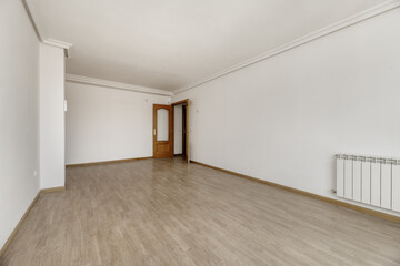 Empty living room of a detached house with doors to other rooms, wooden floors, white aluminum radiator, plaster moldings on the ceiling and white painted walls