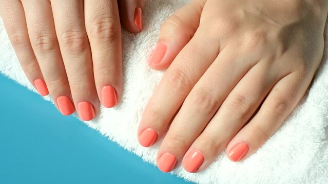 Female hands with pink manicure on a towel on blue background close-up top view.
