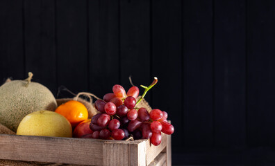 Orange fruits, grapes, apples, cantaloupe placed on a wooden table, black and dark background.