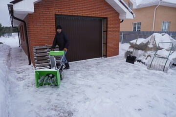 A man cleans snow in the winter in the courtyard of the house,  man cleaning snow with a snow blower