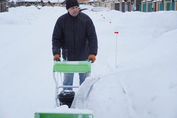 A man cleans snow in the winter in the courtyard of the house,  man cleaning snow with a snow blower