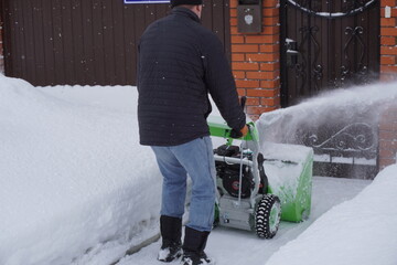 A man cleans snow in the winter in the courtyard of the house,  man cleaning snow with a snow blower