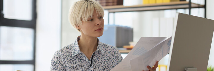 Curious blonde woman compares information reading papers
