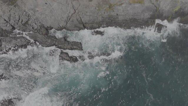 Plano a&eacute;reo zenital desde drone de mar picado con olas con mucho viento chocando contra rocas en la costa. d-log 60fps.
