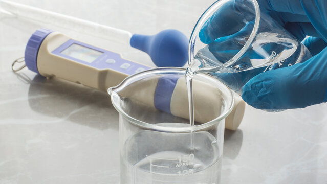 hand with glove pouring water into a beaker. water quality test. Water ph measuring device on the table