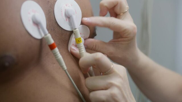 Close up of cardiologist putting sensors for holter monitoring on patient with heart disease. African American man during electrocardiography in cardiology room. Functional rehabilitation in hospital.