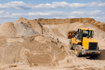 Yellow excavator unloading sand on working at gravel plant. Concept heavy machinery of construction industry