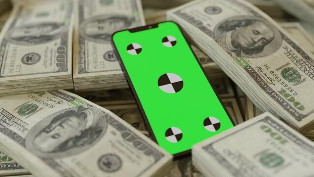 Stacks upon stacks of one hundred dollars and a phone with green screen in the middle