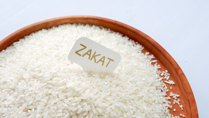 Fototapeta na wymiar ZAKAT word write in white small paper, rice grain in wooden tray on white background. Muslim concept for zakat property.