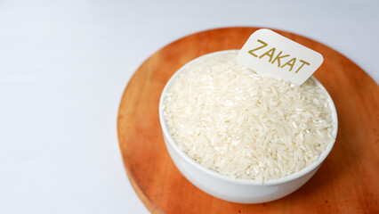 ZAKAT word write in white small paper, rice grain in bowl on white background. Muslim concept for zakat property.
