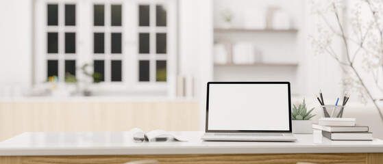 A white-screen laptop mockup and accessories on a white tabletop in a modern, white living room.