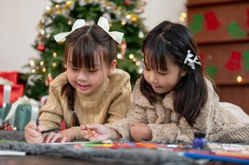 A cute young Asian girl is having fun with her sister on Christmas, enjoying making Christmas cards.