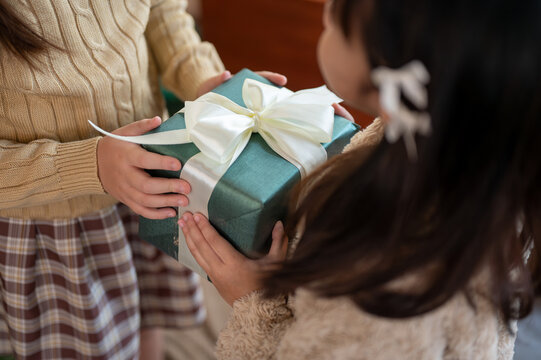 Close-up image of a young girl giving a Christmas gift to her friend or sister. Merry Christmas