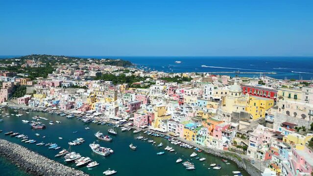 Impressive aerial truck left and pan right shot from Panoramica sulla Corricella on Procida Island (Isola di Procida) of the blue Tyrrhenian Sea in the Gulf of Naples with breakwater, buildings, boats