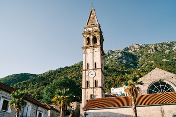 Fototapeta na wymiar Bell tower of the Church of St. Nicholas in Perast against the backdrop of sunny green mountains. Montenegro