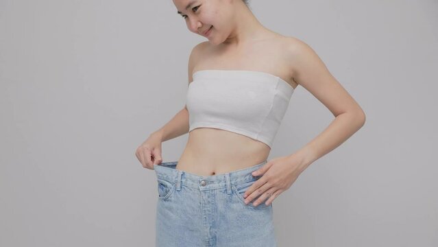 Happy Asian woman  is showing her old oversized jeans after successful diet