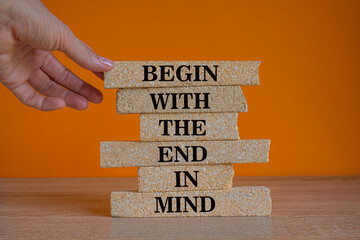 Begin in end of mind symbol. Concept words Begin with the end in mind on brick blocks. Beautiful wooden table orange background. Businessman hand. Business begin in end of mind concept. Copy space.