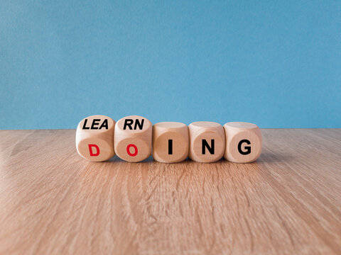 Learning by doing concept. Turned a dice and changes the red word learning to doing, or vice versa. Beautiful wooden table blue background. Copy space.