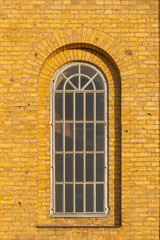 Fototapeta na wymiar A large wooden arched white window on an old yellow brick wall of a 19th century church facade.