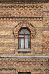 Old wooden arched brown window on an old brick wall of a 19th century building facade.
