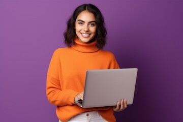 Naklejka premium A girl with a laptop in an orange sweater on a solid purple background.
