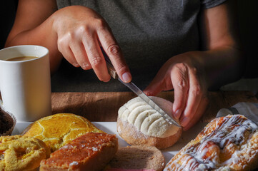 Woman's hand taking a piece of Mexican sweet bread from a white plate on a wooden table. Concept of hands handling food, cutting a white CONCHA with a knife, front view, horizontal.