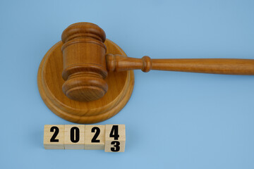Wooden gavel and numbers 2023 and 2024 on wooden cubes on blue background. New laws in year 2024.