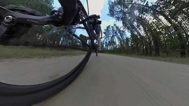 Bicyclist rides MTB bike along sandy road in forest. Cyclist pedals mountain bicycle, rear wheel view. Chain drive, rear derailleur with cassette. Gearshift. Jockey wheels. Low angle Fisheye lens