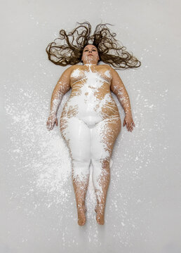 female sexy plus size, fat, overweight, chubby bodypainting nude woman in white color painted decorative, long brown curly hair, lying on the designed floor in the studio