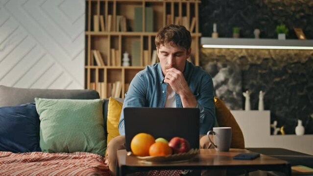 Anxious man looking laptop drinking coffee home late evening. Tired freelancer