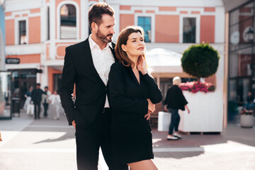 Beautiful fashion woman and her handsome elegant boyfriend in black suit. Sexy brunette model in jacket. Fashionable smiling couple posing in street. Brutal man and female outdoors