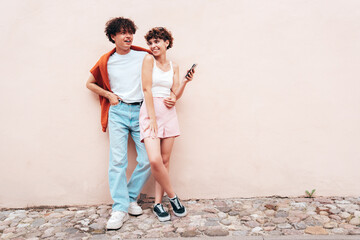Young smiling beautiful woman and her handsome boyfriend in casual summer clothes. Happy cheerful family. Female having fun. Couple posing in street at sunny day. Near  wall. Having tender moments