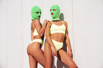 Two beautiful sexy women in green underwear. Models wearing bandit balaclava mask. Hot seductive female in nice lingerie posing in the street at sunny day. Crime and violence. Perfect body