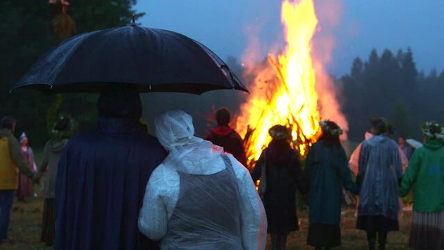 hand held wide shot of people in raincoats and with umbrellas lined up around a big bonfire