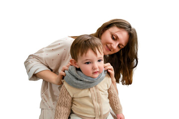 Mother puts a warm scarf on the toddler baby, isolated on a white background. Woman mom dressing warm clothes on child for winter walk in cold weather. Kid aged one year and three months